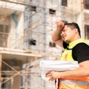 A construction worker stands in the sun wiping sweat from forehead