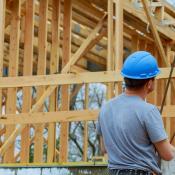 A construction worker in a blue hard hat looks over at home that is under construction