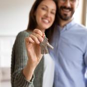 A young couple smiles and holds up a house key.