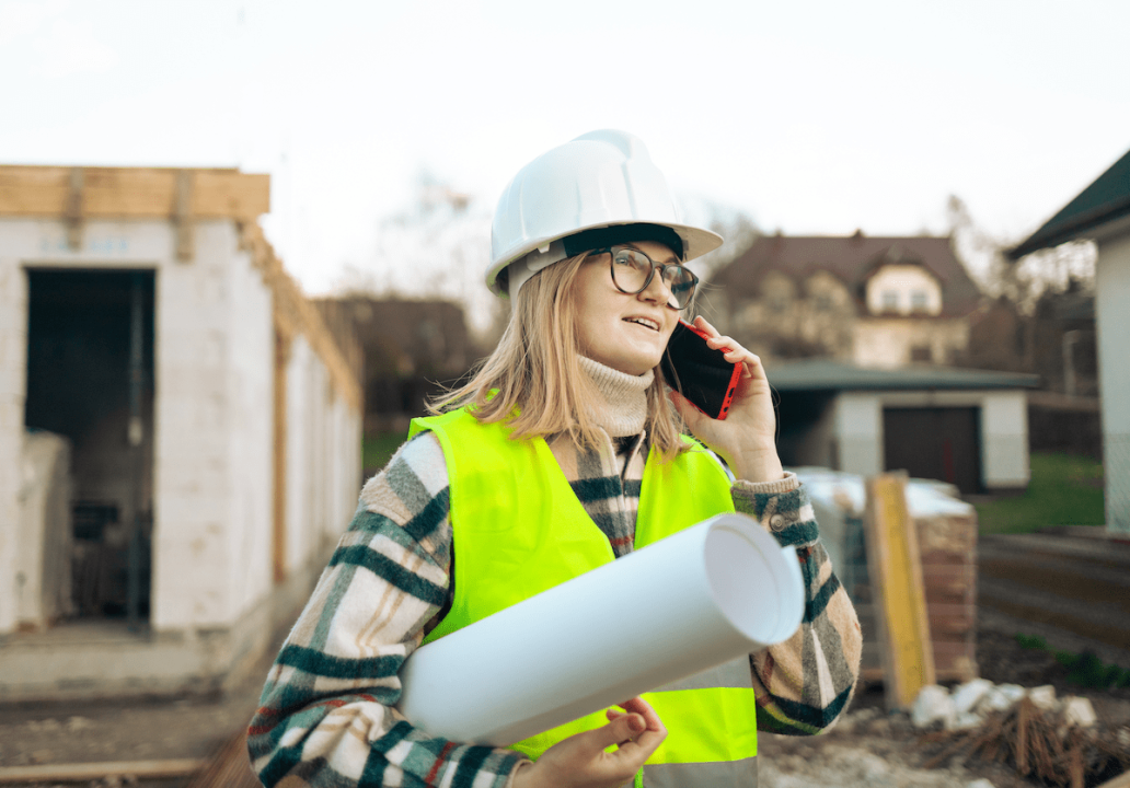 A woman construction worker holding a roll of house plans on a jobsite